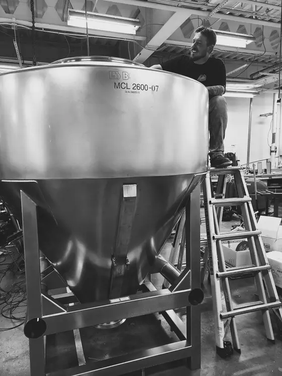 Wetzel Welding technician on a ladder servicing a large stainless steel conical process hopper