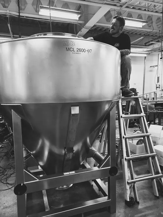 Wetzel Welding technician on a ladder servicing a large stainless steel conical process hopper