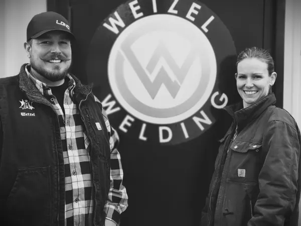 Brennon and Katy Wetzel, owners of Wetzel Welding, standing in front of the company logo at their Salem, Utah shop